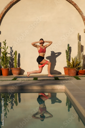 pilates instructor standing in pilates pose on mat near swimming pool