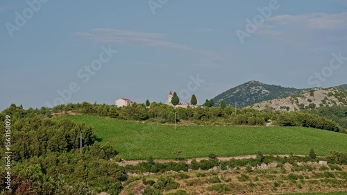 Small old church on the hilltop surrounded by lush vineyards and pine trees in Slivno Ravno Croatia peaceful rural countryside view with mountains in the distance and blue sky above
