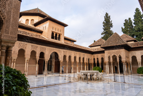 The interior courtyard of the Alhambra in Granada, Spain, highlighting its intricate Moorish architectural design. Tourists can be seen exploring this historic site.
