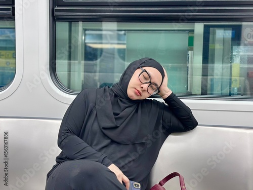 A woman in black hijab peacefully sleeping on a modern LRT train seat, showcasing calm, comfort, and quiet moments during urban commuting in public transportation.