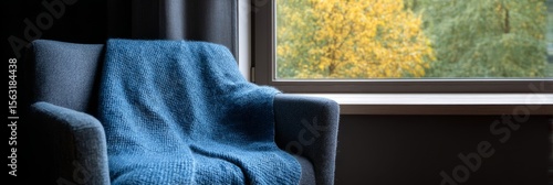 Cozy armchair draped in cerulean knit whispers autumn reveries by the window, ideal for Hygge moments and World Mental Health Day