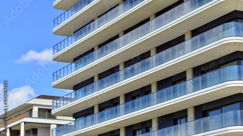 Exterior of a high modern multi-story apartment building - facade, windows and balconies. Modern glass balcony railings.