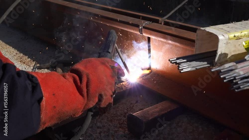 worker welding steel beam with bright sparks in construction site wearing protective gloves and creating metal joint close up industrial craftsmanship repair maintenance safety and technology process