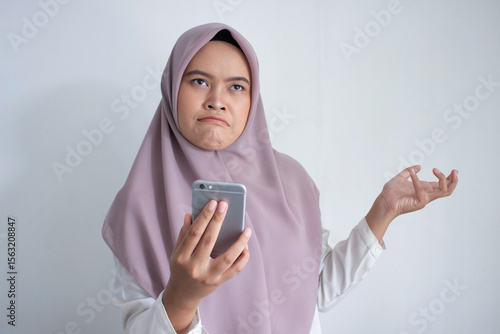 young muslim asian woman wearing a purple hijab a head scarf is looking at her phone. She is upset or confused