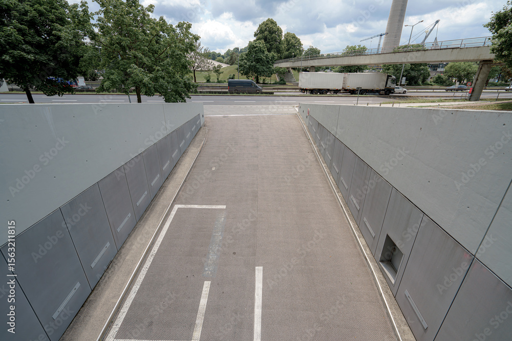 Obraz premium Urban underpass leading to a busy street with trucks and trees during daylight hours