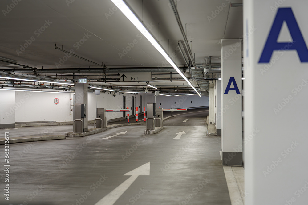 Obraz premium Parking garage interior with directional signs, barriers, and clear exit paths for vehicles at night