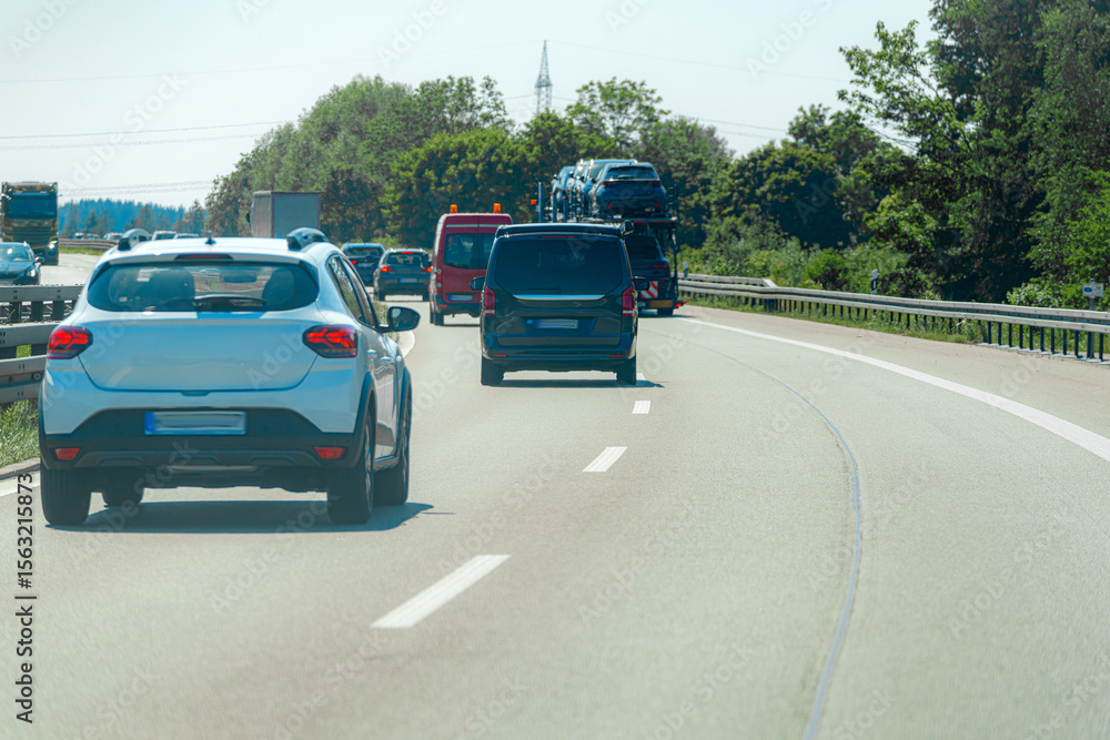 Fototapeta premium Vehicles traveling on a busy highway under bright sunlight with trees lining the road