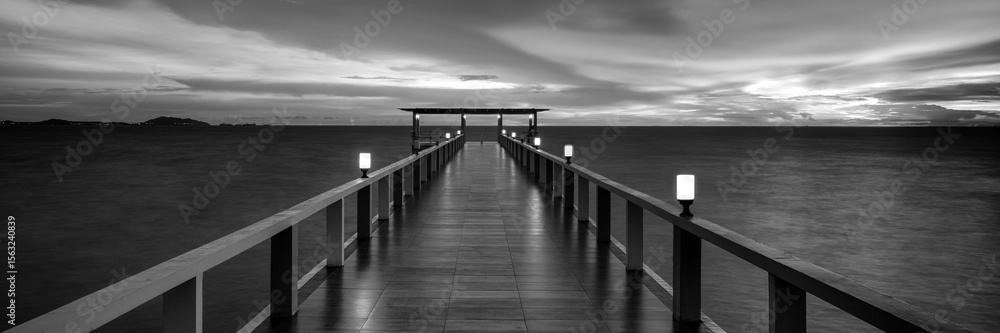 Obraz premium Panoramic image. Wooden jetty on the sea. Dramatic sky with clouds in black and white
