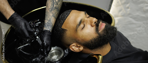 Web banner of tattooed barber holding faucet near sink and african american client in barbershop
