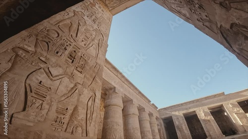 captivating view through a sunlit corridor of an ancient Egyptian temple, showcasing massive stone columns and walls intricately carved with hieroglyphics and pharaoh reliefs.