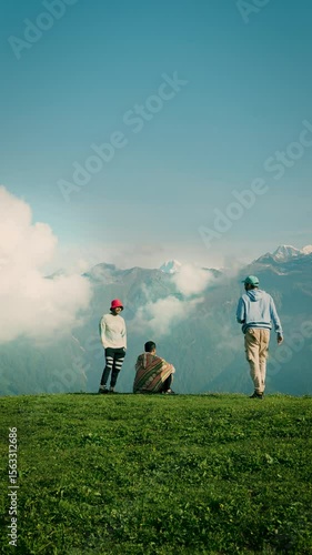 A group of young friends hiking in the countryside. Two men are sitting while the third man is walking. A travel and adventure moment with three friends at Buda Madmaheshwar, Uttarakhand, India.
