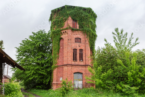 Fotografie Old brick water tower overgrown with creeping plants during rain