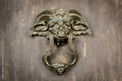 Aged bronze door knocker shaped like mythological creature on antique door