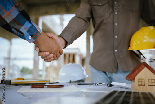 Tablou pe pânză Two builders shaking hands at a construction site, representing a successful agreement and partnership built on trust, cooperation, and a shared goal of developing and growing real estate