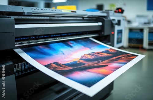 A large-format printer produces a vibrant, high-resolution landscape print featuring mountains and a colorful sky.
