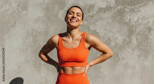 Woman in orange athletic wear smiling outdoors against a concrete wall