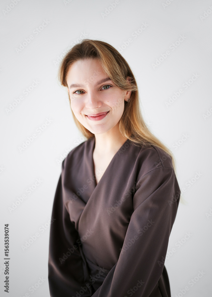 Portrait of a smiling young woman in a brown uniform, possibly a doctor or cosmetologist, looking at the camera on a light background. Portrait of a smiling young woman in a brown uniform, possibly a doctor or cosmetologist, looking at the camera on a light background.