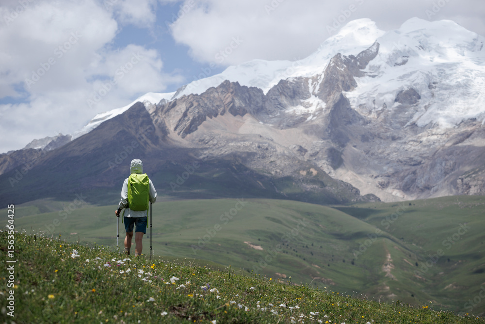 Naklejka premium Backpacking woman hiking on grassland kneeling down show respect to the holy snow capped mountains