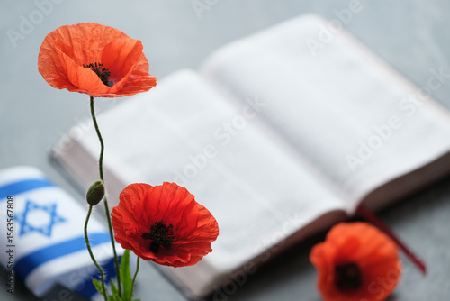 Canvas-taulu Bright orange poppies placed near an open book on a dark surface, Israeli flag a symbol of remembrance and hope