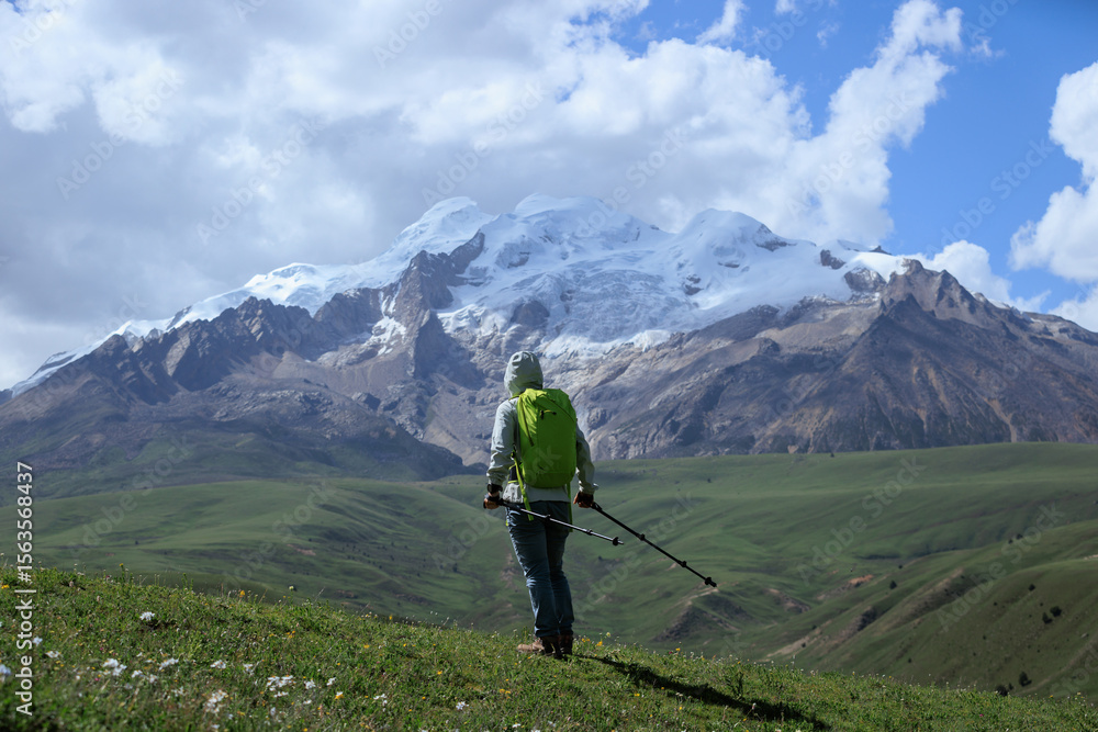 Obraz premium Backpacking woman hiking on grassland and snow capped mountains