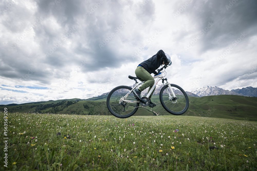 Woman cyclist riding mountain bike on grassland mountains with snow capped mountain in the distance Woman cyclist riding mountain bike on grassland mountains with snow capped mountain in the distance