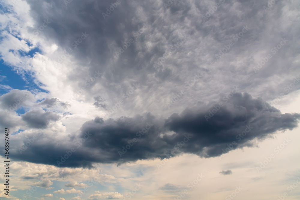 A large dark gray cloud among other cumulus clouds as a change in weather, cloudy weather changing a clear day, approaching rain. A large dark gray cloud among other cumulus clouds as a change in weather, cloudy weather changing a clear day, approaching rain.