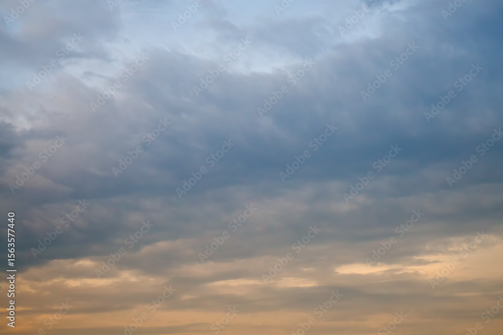 A large blue cloud and the yellow light of the setting sun on the haze in the sky, cloudy weather before sunset in pastel shades. A large blue cloud and the yellow light of the setting sun on the haze in the sky, cloudy weather before sunset in pastel shades.