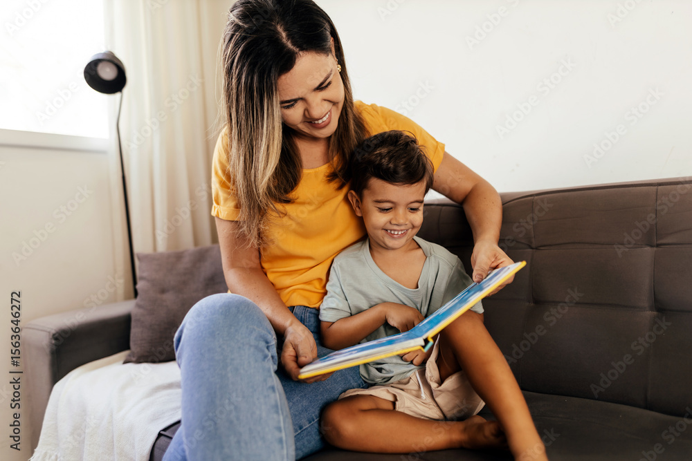 Obraz premium Smiling mother and son enjoy reading a book together on the couch