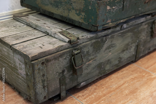 Stacked old wooden ammunition boxes painted in green are on a tiled floor