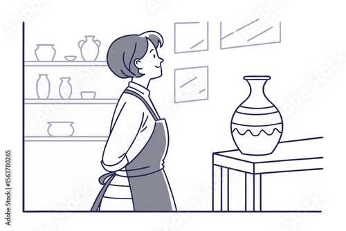 A person wearing an apron looks thoughtfully at a decorative vase displayed on a table in a studio with shelves of pottery