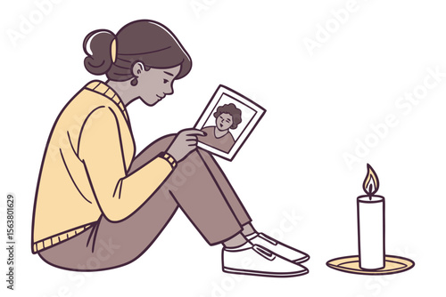 A woman sits on the floor looking at a framed photograph of another person while a lit candle burns nearby