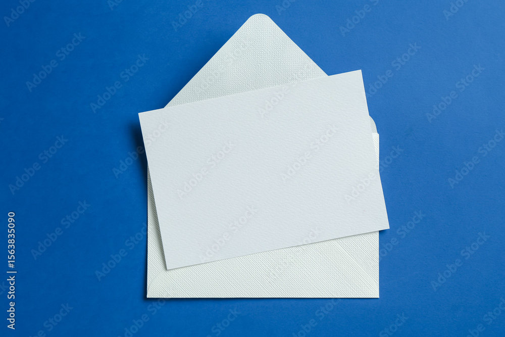 Naklejka premium Blank invitation card and envelope on blue background, top view. Space for design