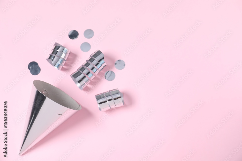 Fototapeta premium Shiny party streamers, confetti and cone on light pink background, top view. Space for text