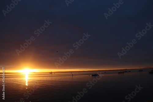 Foto The sun rises above a calm bay, casting a golden glow over wooden picnic tables and tranquil waters, creating a perfect moment of stillness