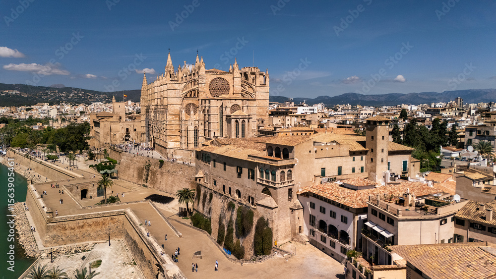 Naklejka premium An aerial view of Palma de Mallorca showcasing its grand cathedral, surrounded by historic buildings and coastal defenses, under a clear blue sky