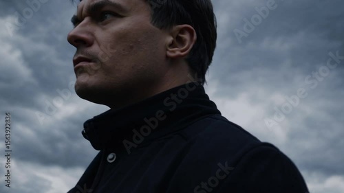 Homme en manteau sombre sous un ciel orageux