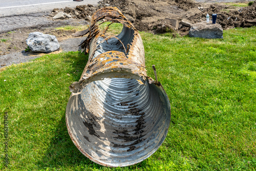 Infrastructure photo of rusted out corrugated metal pipe, CMP, drainage culvert, that has been removed from the ground and being replaced with a new pipe.