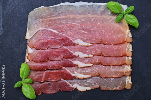 sliced ​​smoked ham on a black board and basil leaves