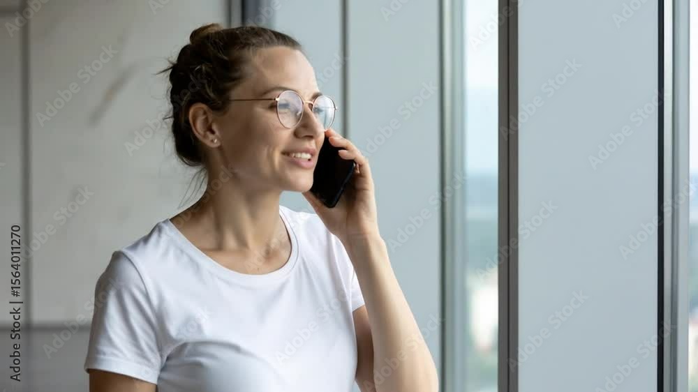 Woman talking on a phone, smiling and looking out a window Woman talking on a phone, smiling and looking out a window