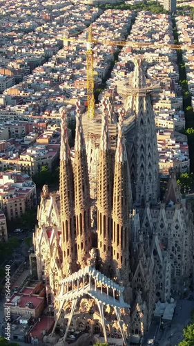 Iconic aerial drone video of Sagrada Familia cathedral in Barcelona at golden hour, intricate spires and cranes rising above sprawling city, casting dramatic shadows. Deep focus, cinematic lens