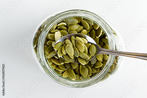 Shelled pumpkin seeds on a spoon over a jar of pumpkin seeds.