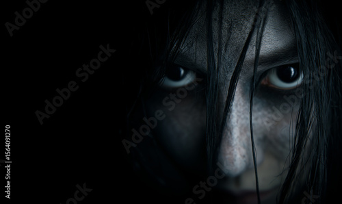 close-up of evil black eyes scary young woman with black hairs falling on her pale face; concept of horror, halloween, fear, paranormal event / promotion; black background; copy space