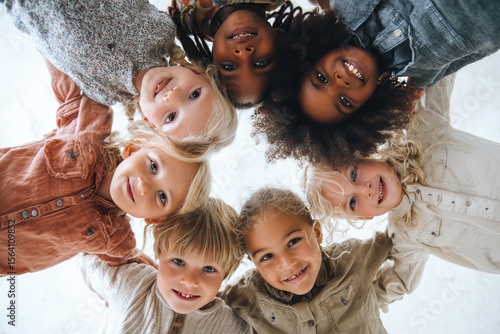 A diverse group of smiling children huddle together in a circle, arms around each other's shoulders, viewed from a low angle