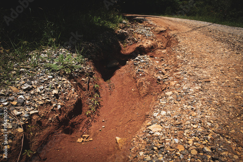 an example of erosion, gully or rill erosion, caused by the movement of water across the red clay soil topped with crushed stone surface