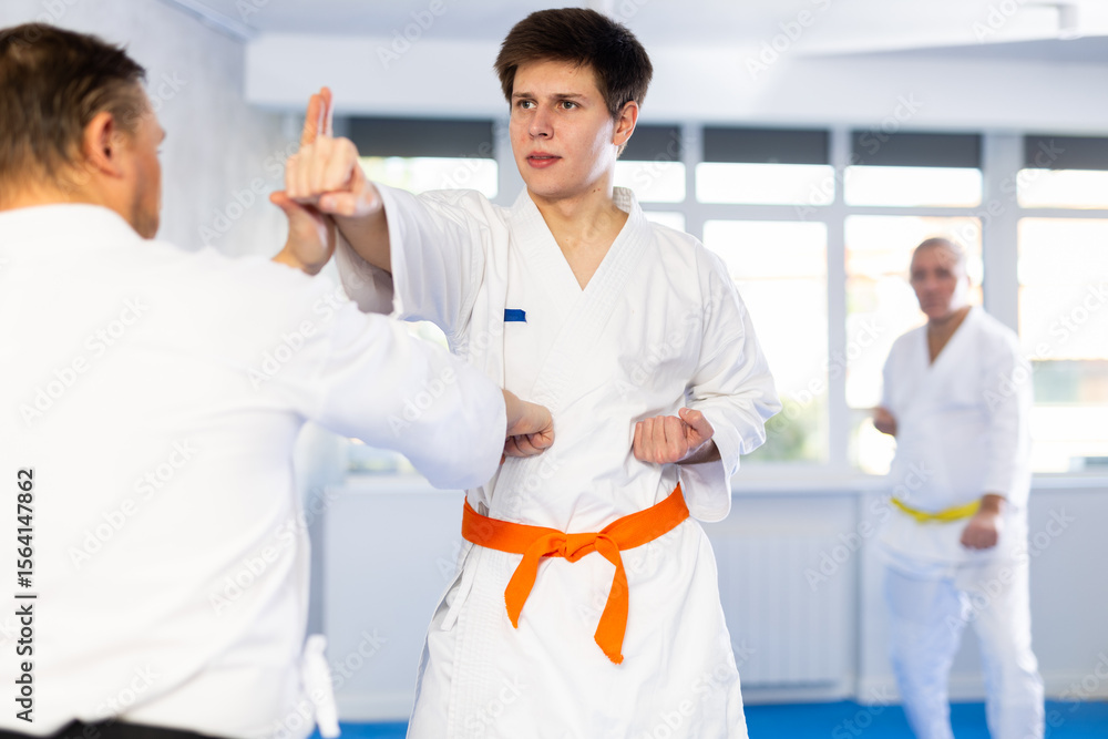 Obraz premium Concentrated young guy in kimono honing punching techniques during kumite with male opponent at karate training session