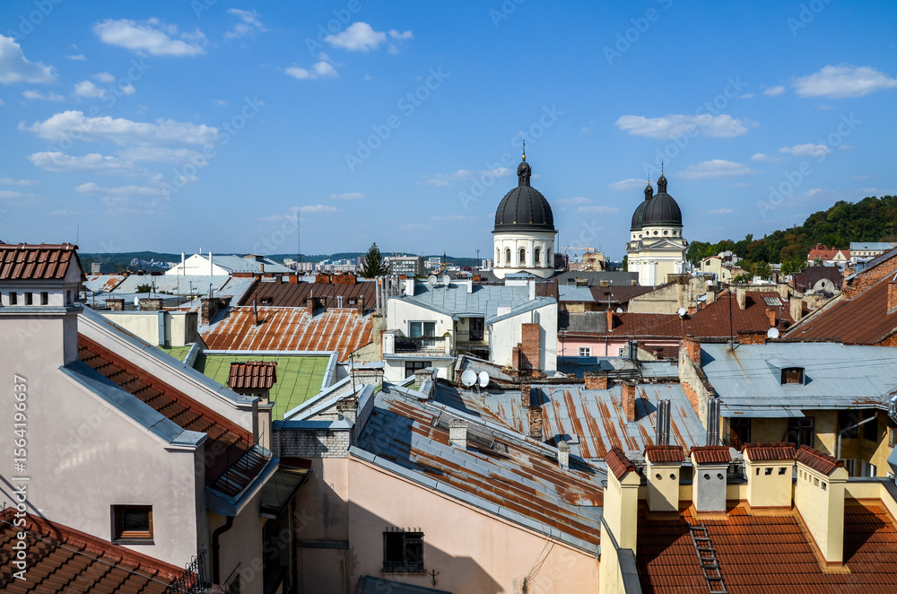Fototapeta premium Panoramic view of Lviv's rooftops with diverse textures and colors, dominated by prominent Transfiguration church domes against a clear blue sky