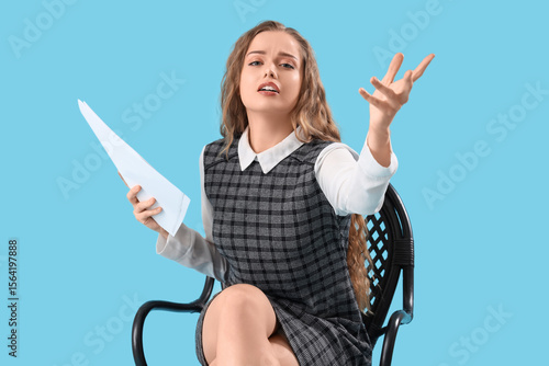 Fotografie Beautiful actress with film script in chair on blue background