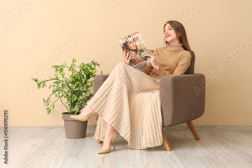 Tableau sur toile Beautiful woman reading fashion magazine in armchair near beige wall