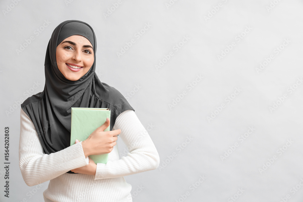 Beautiful Muslim woman with book on grey background Beautiful Muslim woman with book on grey background