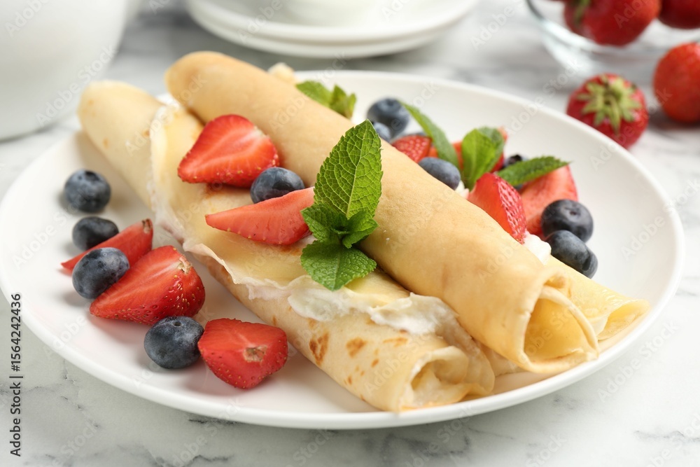 Tasty crepes with cream, berries and mint on white marble table, closeup Tasty crepes with cream, berries and mint on white marble table, closeup